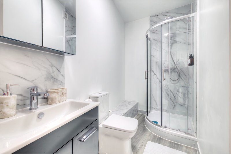 Modern bathroom with white sink, dark vanity, marble backsplash, toilet, and shower enclosure