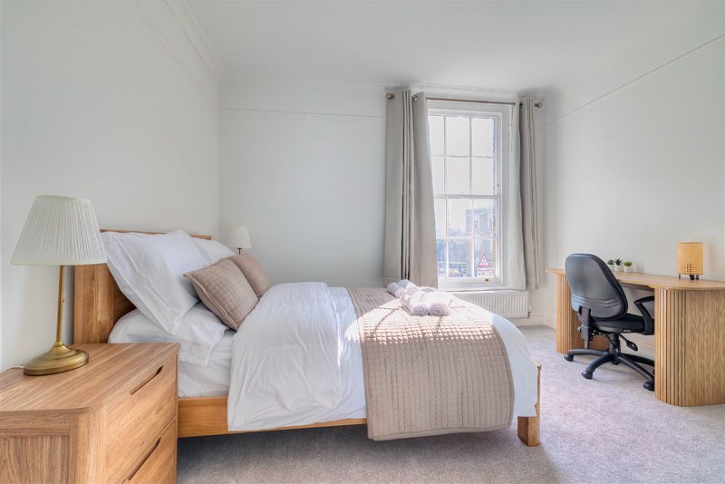 Bright bedroom with double bed, wooden nightstands, desk chair and window with curtains