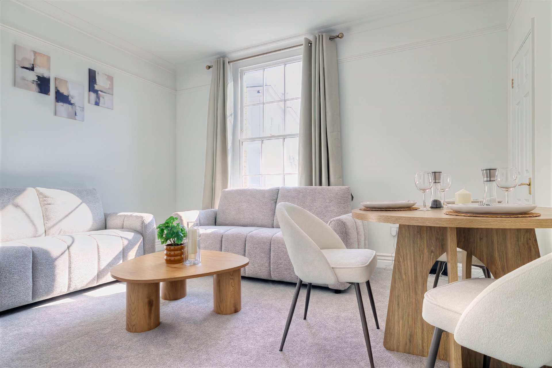 Bright living room with gray sofa, wooden furniture, armchair, and large window with curtains