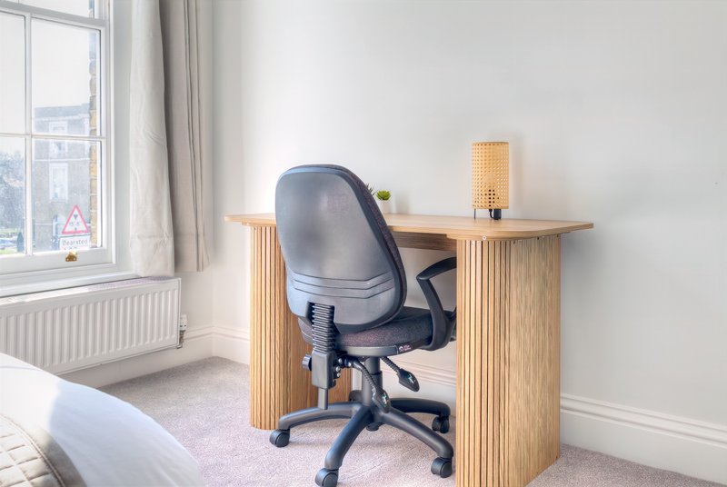 Bright bedroom workspace with wooden desk, black office chair, and window with city view