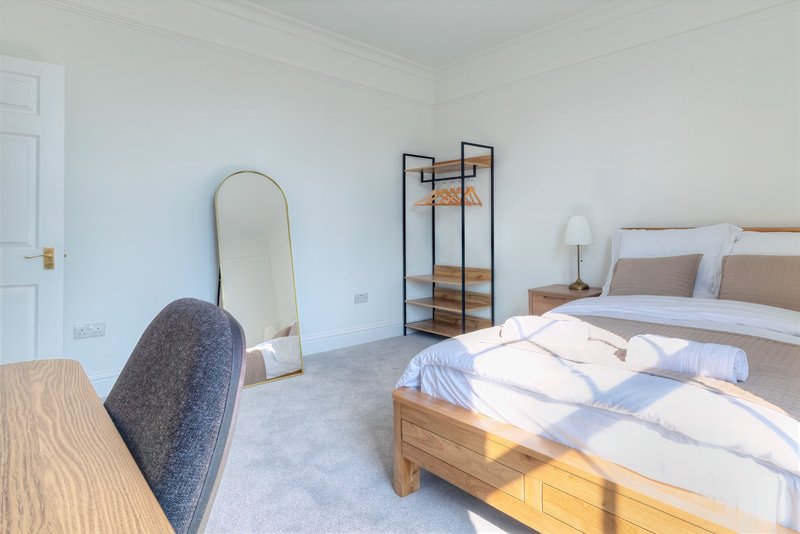 Bright bedroom with wooden bed, desk, mirror, shelving unit and white bedding