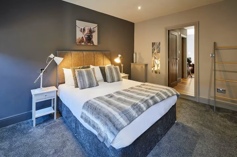 Modern bedroom with gold headboard, striped bedding, white nightstand and grey carpet flooring