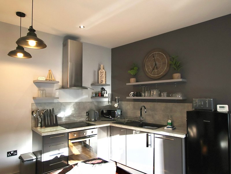 Modern kitchen with white cabinetry, stainless steel appliances, pendant lights, and gray accent wall