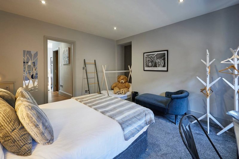 Spacious bedroom with double bed, blue accent chair, decorative ladder and white coat stand