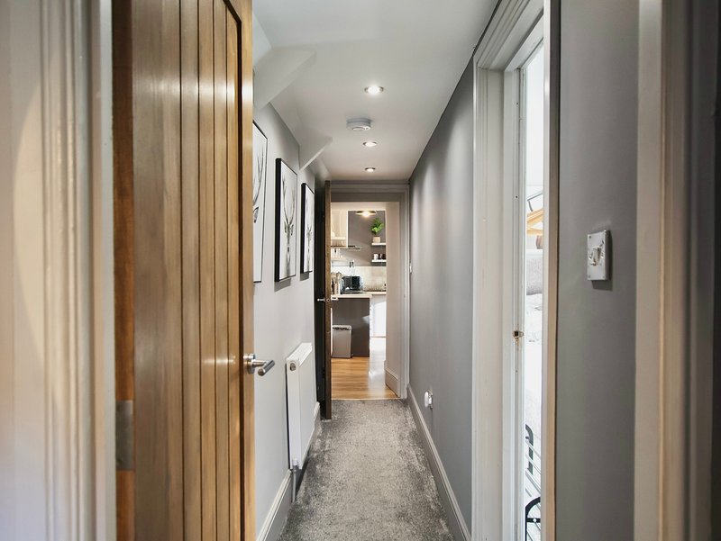 Modern hallway with wooden doors, recessed lighting, and view toward kitchen area