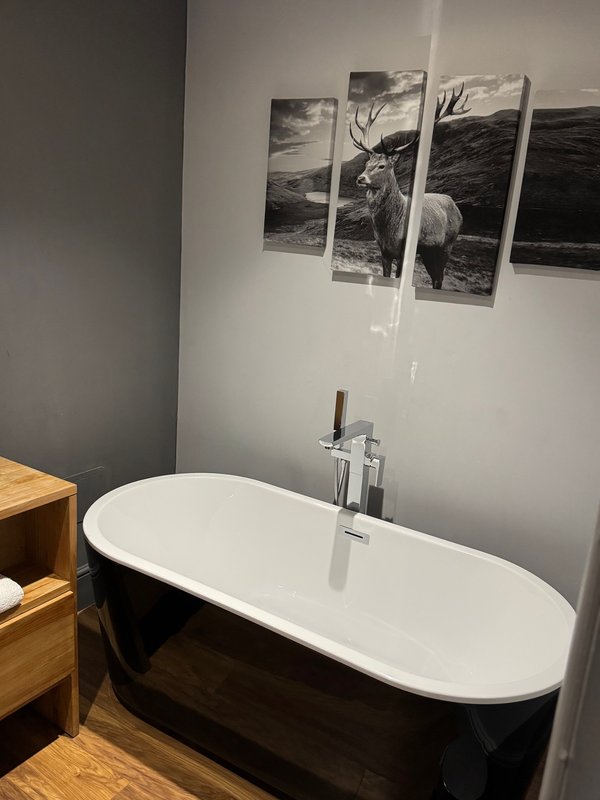 Modern bathroom with black and white freestanding bathtub, wooden vanity, and wall art