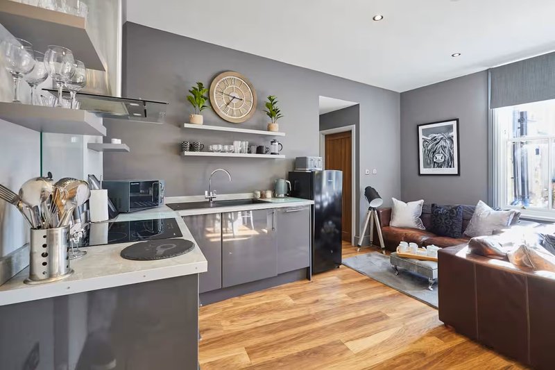Open-plan kitchen and living area with gray cabinetry, wooden flooring, and brown leather sofa