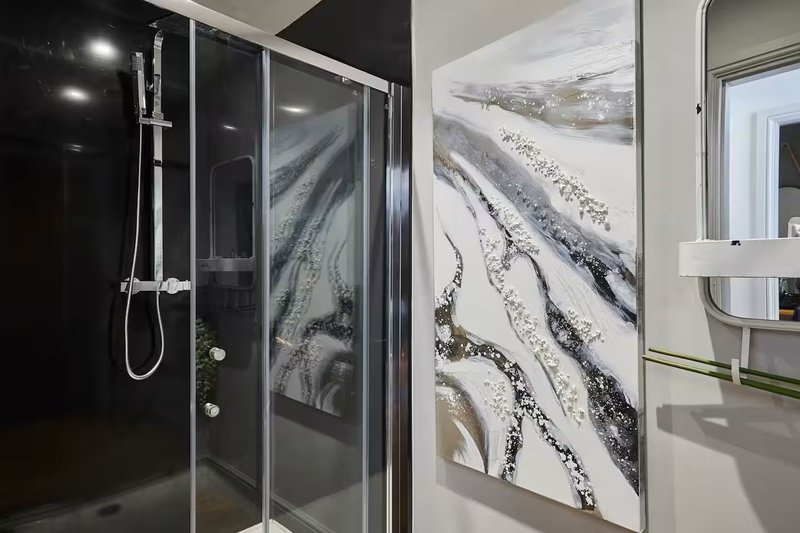 Modern bathroom with black tile shower enclosure and abstract wall art