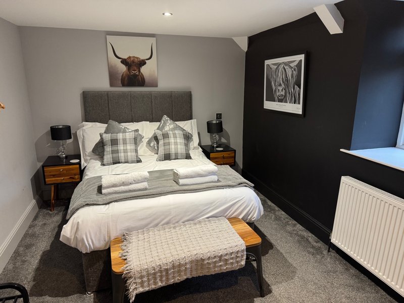 Modern bedroom with grey upholstered bed, plaid pillows, wooden nightstands, and black accent wall