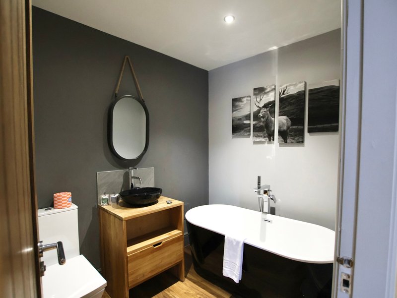 Modern bathroom with black freestanding bathtub, wooden vanity sink, oval mirror and framed wall art