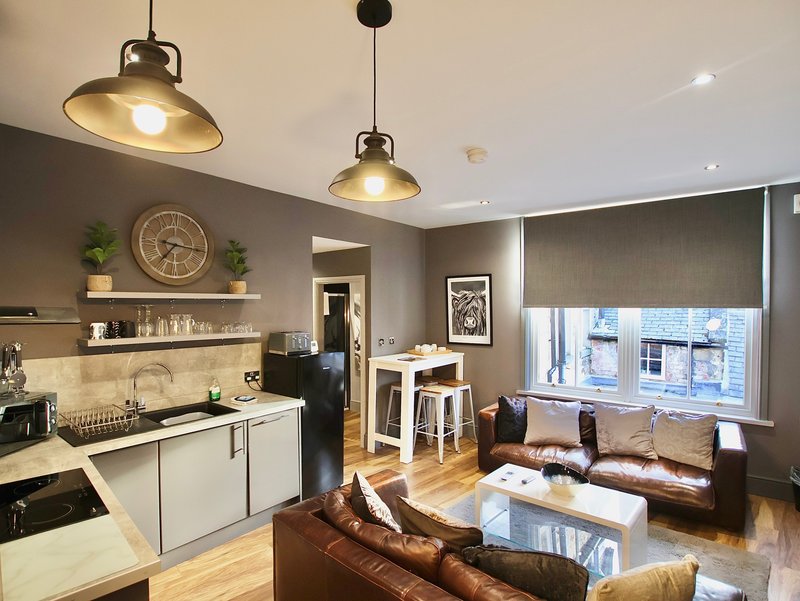 Open-plan kitchen and living room with pendant lights, white cabinetry, brown leather sofa and dining area