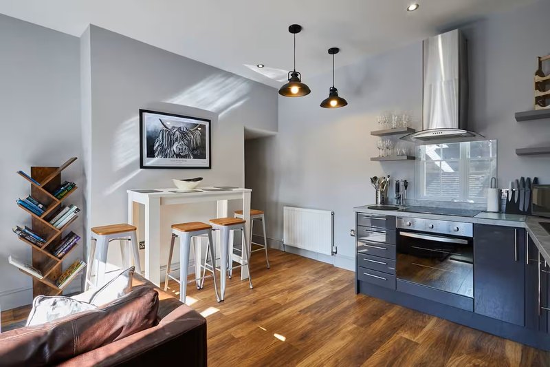 Modern open-plan kitchen and dining area with wooden flooring, pendant lighting, and stainless steel appliances