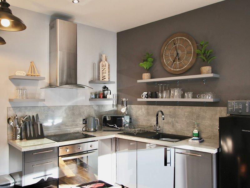 Modern kitchen with stainless steel appliances, open shelving, and grey accent wall