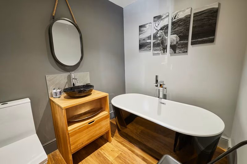 Modern bathroom with freestanding black bathtub, wooden vanity, round mirror and wall art