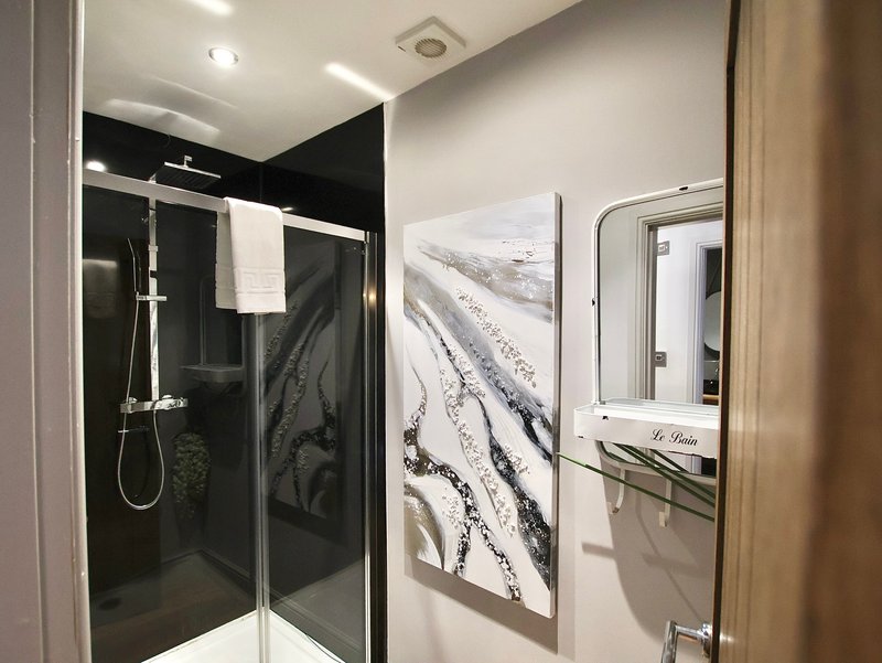 Modern bathroom with black walk-in shower, white towel rail, and landscape artwork on wall