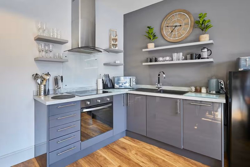 Modern kitchen with blue cabinetry, stainless steel appliances, wooden flooring and wall shelving