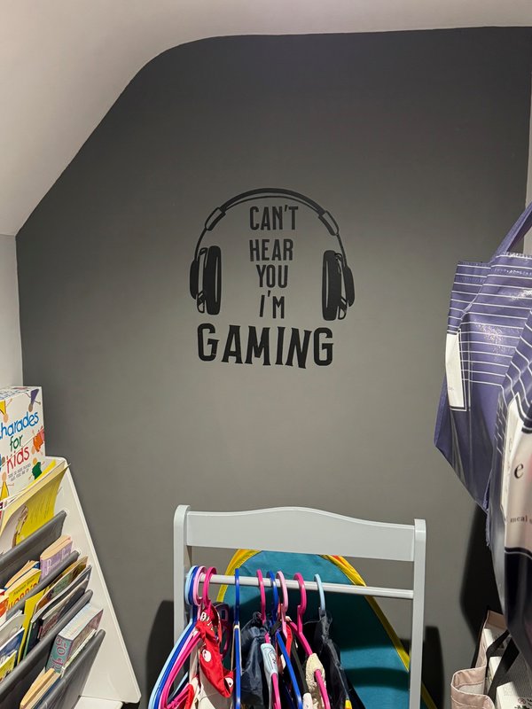 Bedroom corner with white chair, gaming wall decal, and clothing rack