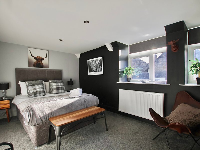 Modern bedroom with grey upholstered bed, wooden bench, black accent wall and seating area