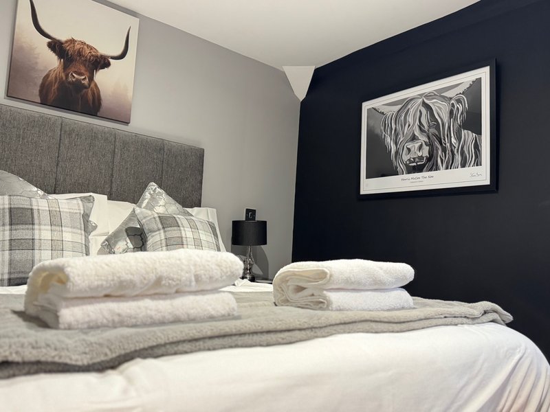 Modern bedroom with double bed, grey headboard, white bedding, folded towels, and framed artwork on walls