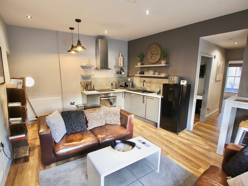 Open-plan living and kitchen area with leather sofa, white coffee table, and fitted kitchen with black appliances