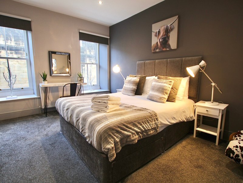 Modern bedroom with double bed, striped bedding, dark headboard, desk and windows