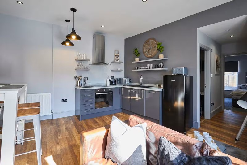 Open-plan kitchen and living area with dark blue cabinetry, stainless steel appliances, wooden flooring, and seating area