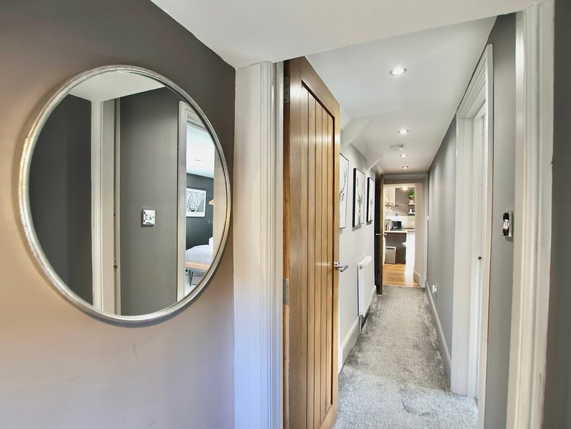 Modern hallway with round illuminated mirror, wooden door frame, and carpeted flooring