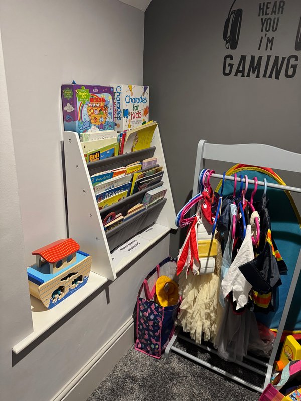 Child's bedroom with wall-mounted magazine rack, clothing rack with colorful garments, and gaming-themed wall text.