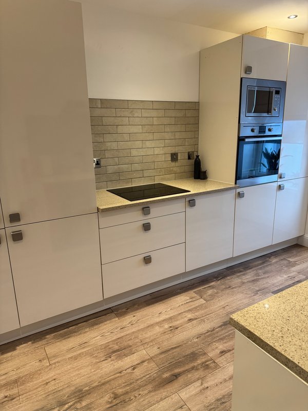 Modern white kitchen with brick backsplash, built-in oven, wooden flooring and stone countertops