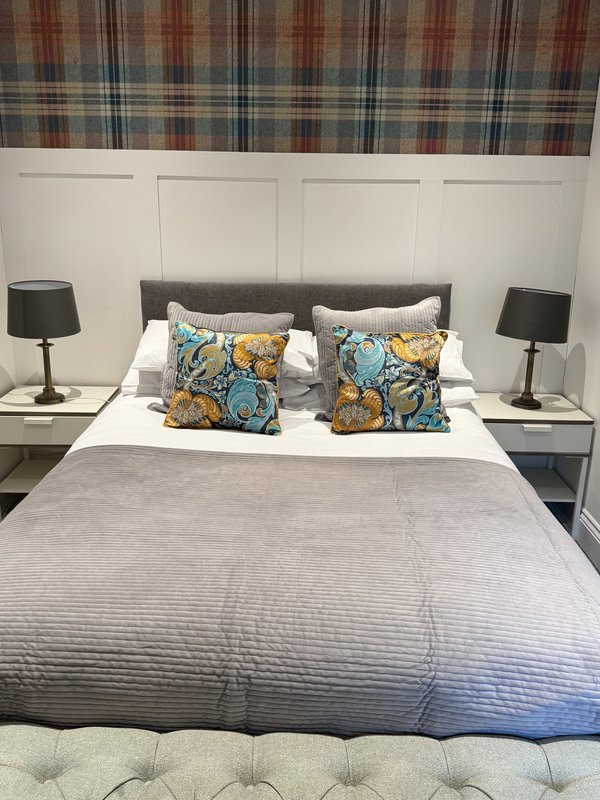 Modern bedroom with grey upholstered bed, patterned cushions, bedside lamps and panelled headboard