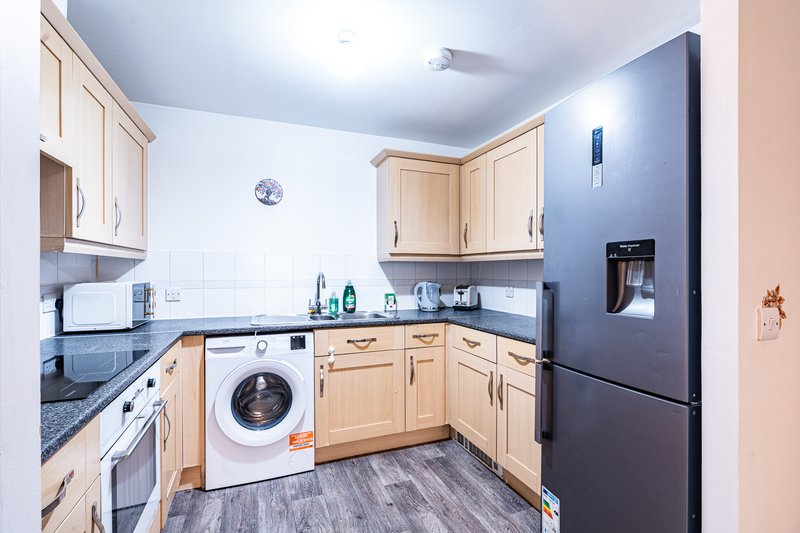 Modern kitchen with wooden cabinets, washing machine, black fridge and white countertops