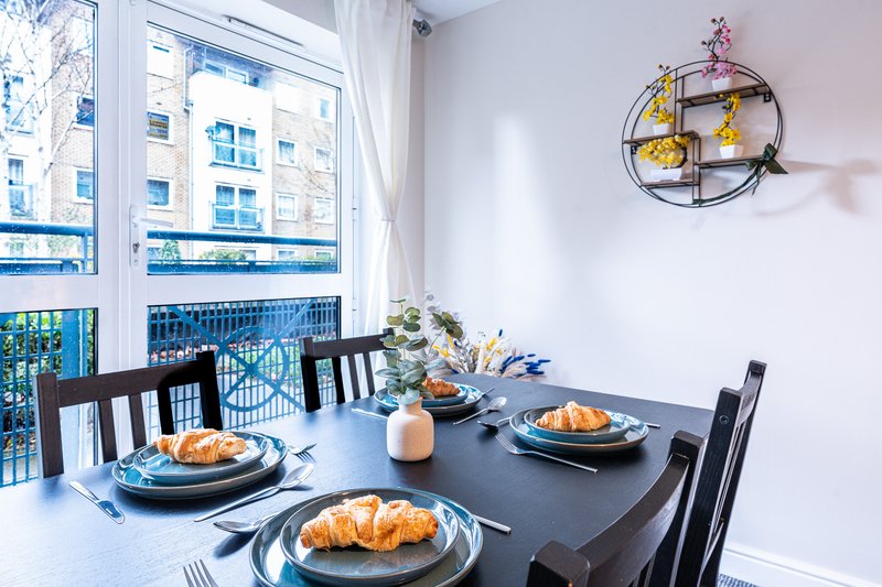 Modern dining room with black table, croissants plated, blue dishes, wall shelf decor and large windows