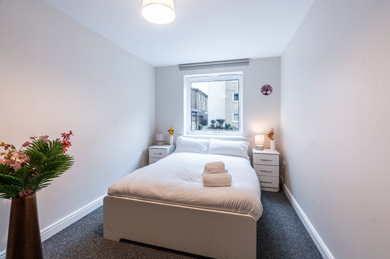 Compact bedroom with double bed, white bedding, small window, and potted flowers on side table