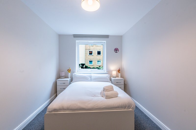 Narrow bedroom with single bed, white bedding, small nightstands, and window view
