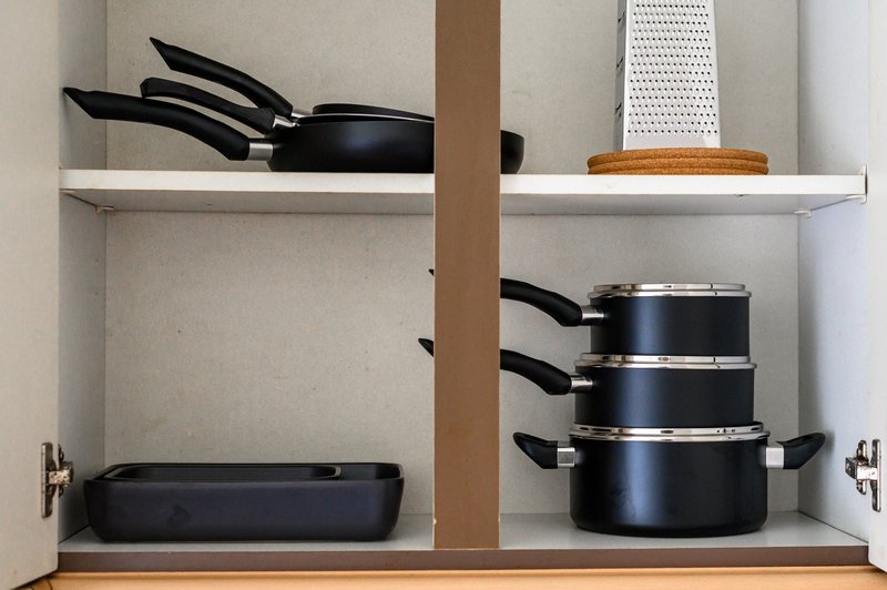 Kitchen cabinet interior with black cookware, pans, and cooking utensils on shelves