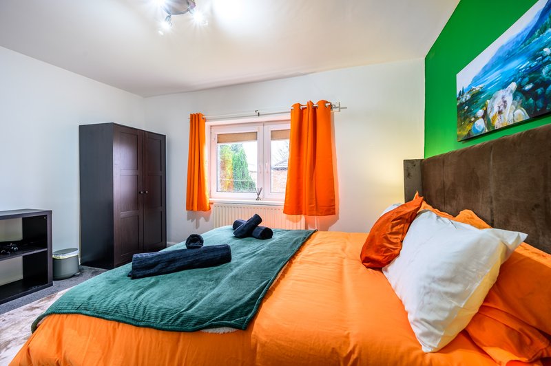 Bright bedroom with orange bedding, teal quilt, orange curtains and green wall accent