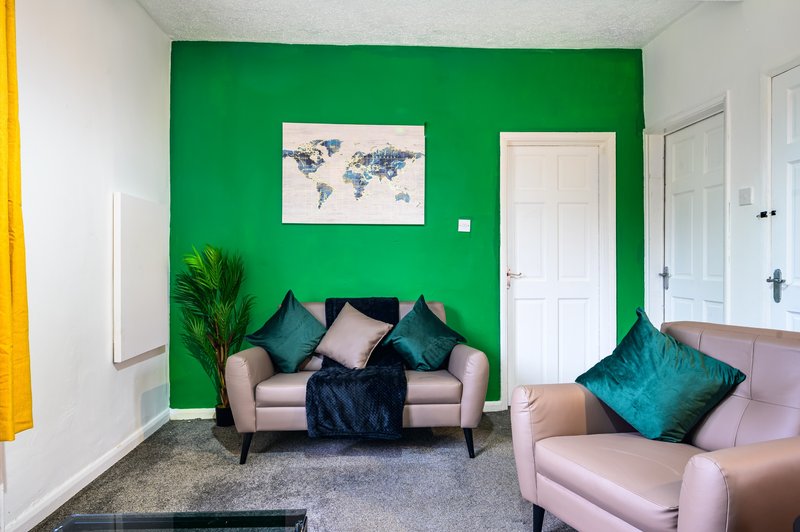 Bright living room with green accent wall, pink sofas, teal cushions, and world map artwork