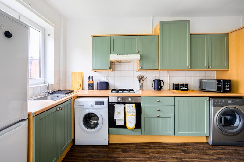 Modern kitchen with green cabinetry, wooden countertops, washing machine, and integrated appliances