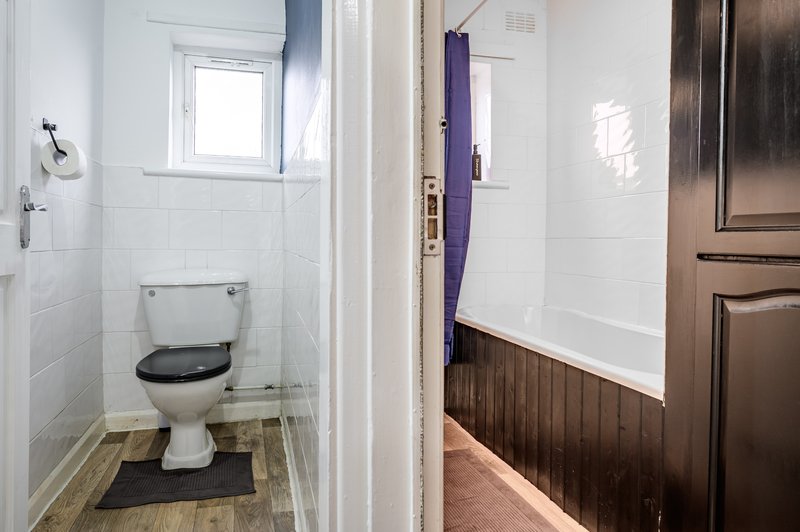 Small bathroom with toilet, window, white tiles and wooden floor mat