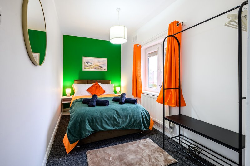 Modern bedroom with green accent wall, teal bedding, orange curtains and round mirror