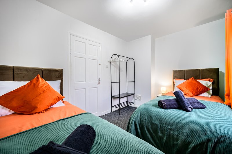 Bright bedroom with two beds, orange and teal bedding, wooden headboards, wardrobe