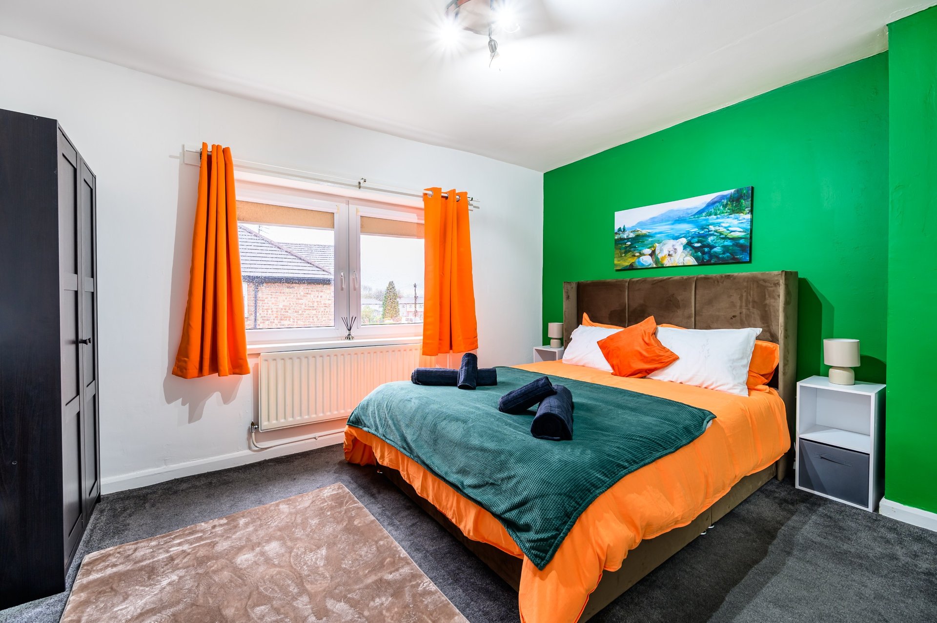 Bright bedroom with green accent wall, double bed with orange bedding, window with orange curtains