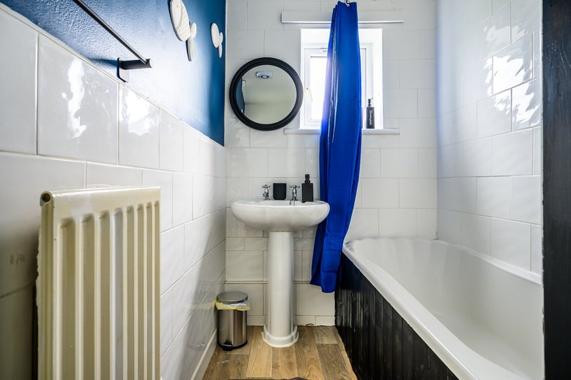 Compact bathroom with white tiles, pedestal sink, bathtub, radiator and blue shower curtain