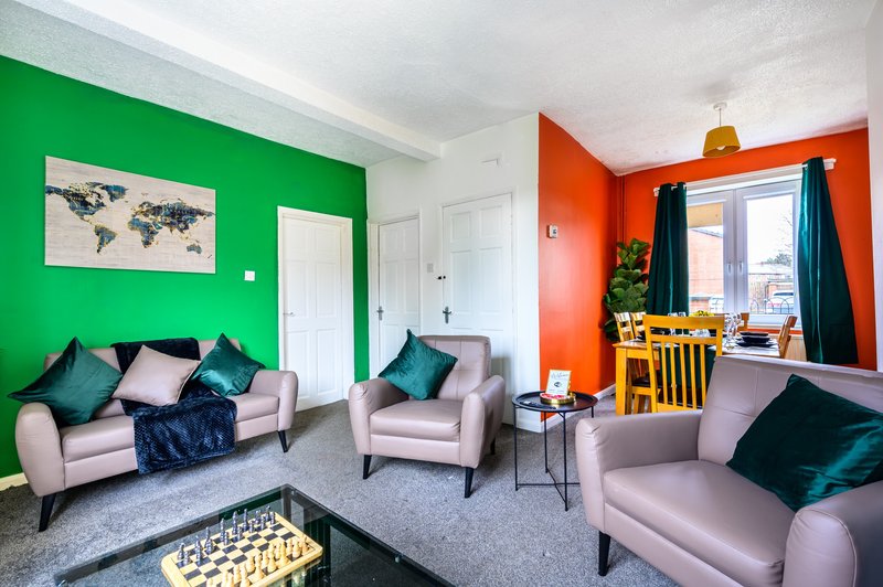 Colorful open-plan living area with green and orange accent walls, gray upholstered seating, and window views