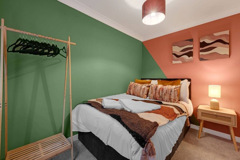 Modern bedroom with double bed, green and orange walls, wooden clothing rail and bedside table