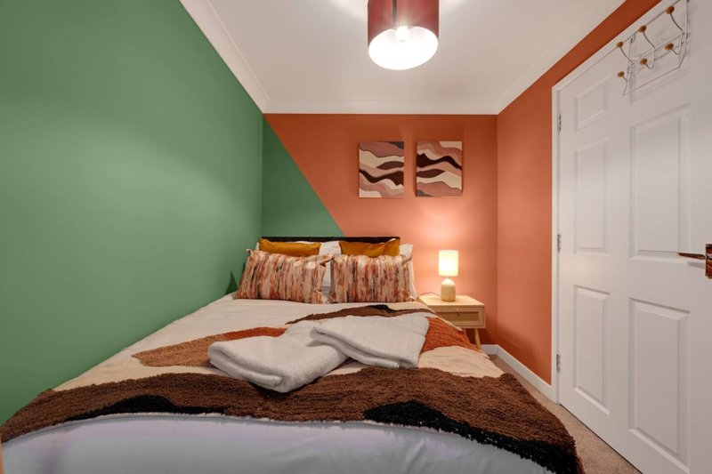 Compact bedroom with double bed, green and orange walls, bedside lamp and white wardrobe