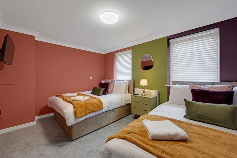 Multi-bed bedroom with coral and green walls, three single beds, bedside tables and warm lighting