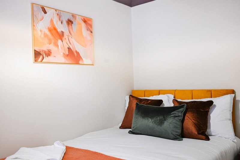 Modern bedroom with orange upholstered bed, white bedding, decorative cushions and abstract wall art