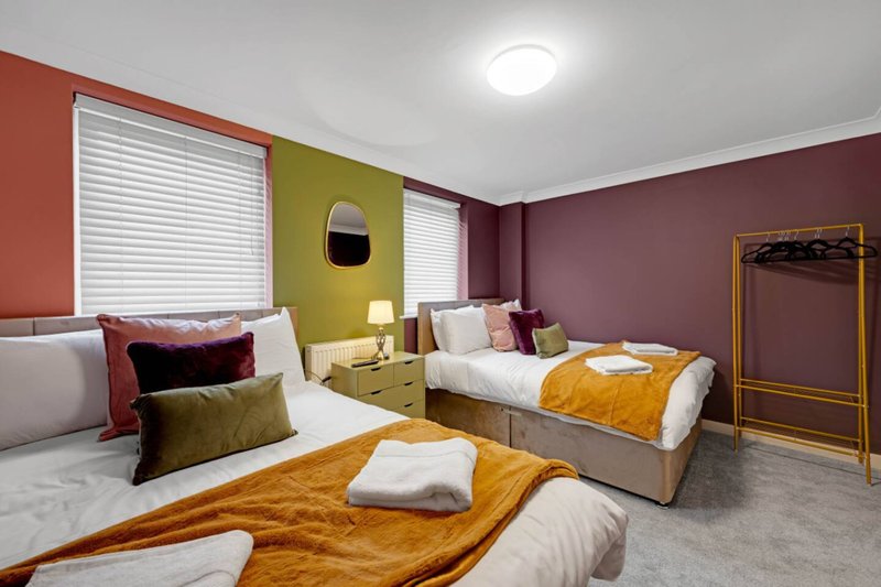 Colorful bedroom with three beds, gold throws, decorative pillows and white roller blinds