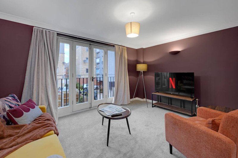 Modern living room with purple walls, orange sofa, TV unit, and balcony doors with city views